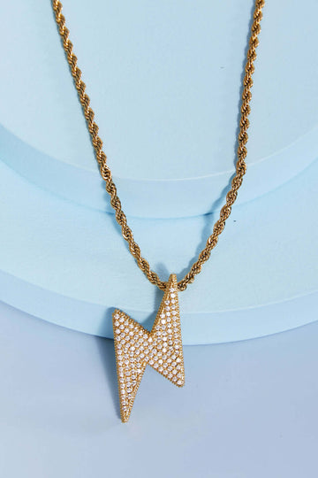 Brass lightning pendant necklace with twisted chain and cubic zirconia detail in flat lay style.