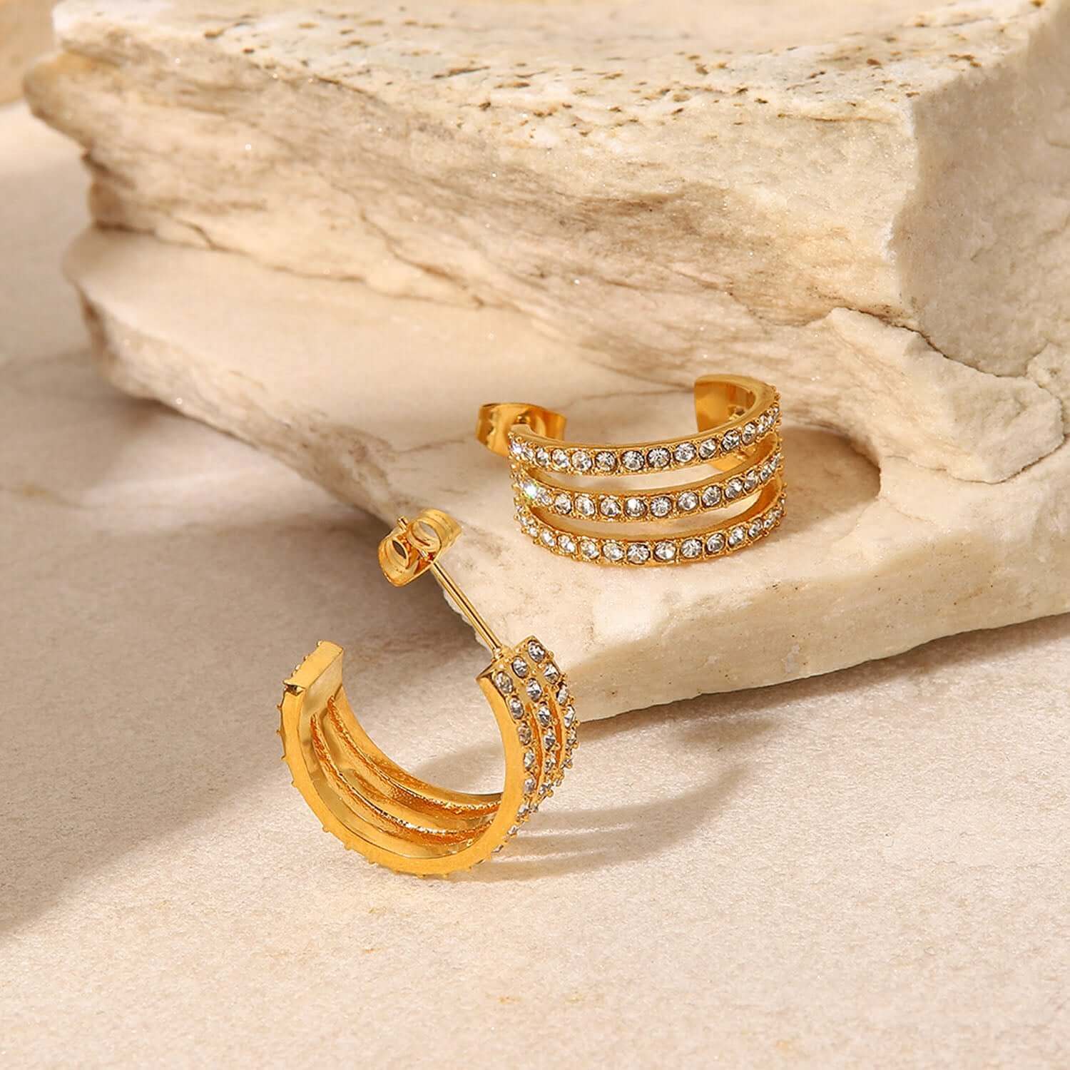 Gold-plated stainless steel C-hoop earrings inlaid with zircon gems displayed on stone background.