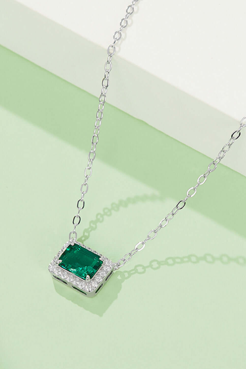 Minimalist lab-grown emerald rectangle pendant necklace in platinum-plated sterling silver with zircon accents on green background.