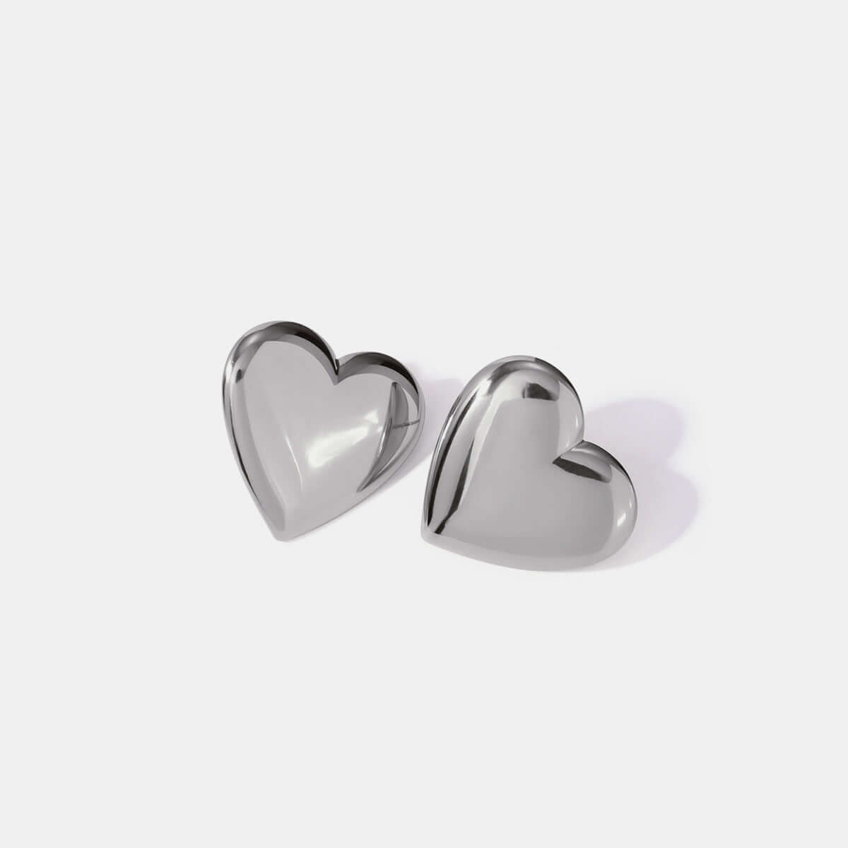 Stainless steel heart-shaped stud earrings with reflective surface on a light background, ideal for adding elegance to any outfit.