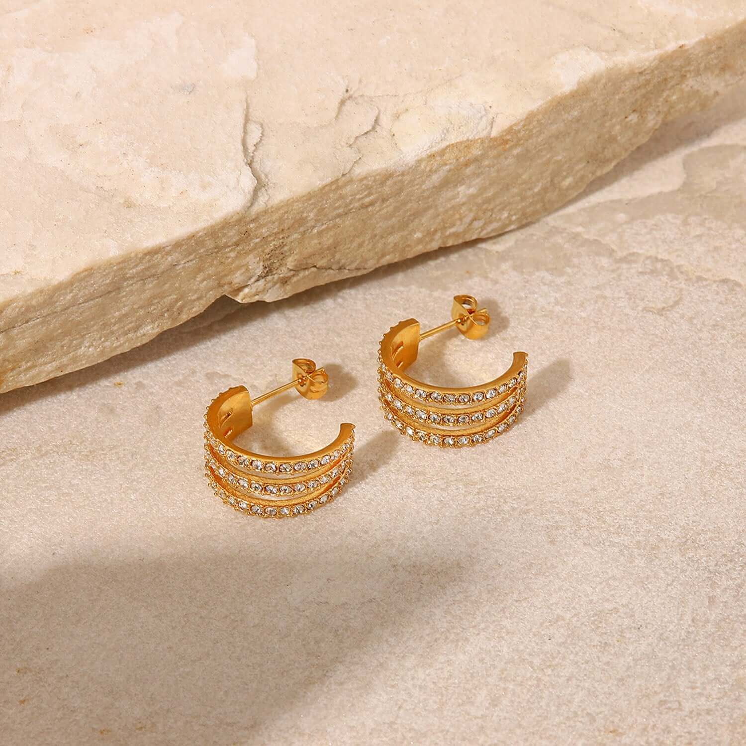 Gold-plated stainless steel C-hoop earrings with inlaid zircon stones, displayed on a stone slab background.