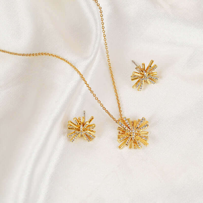 Starburst gold-plated earrings and necklace set with zircon detailing on white fabric background