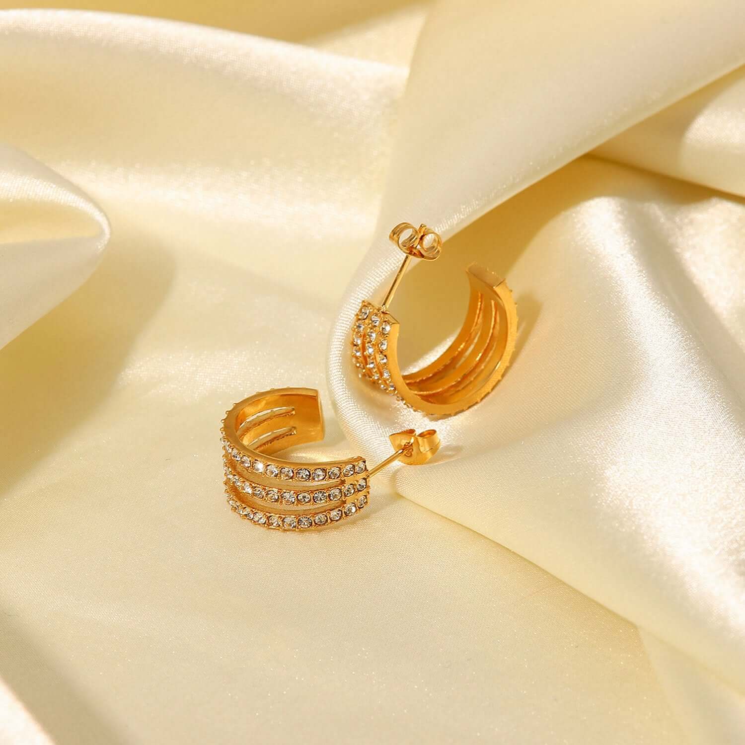 Gold-plated stainless steel inlaid zircon C-hoop earrings displayed on soft satin fabric.