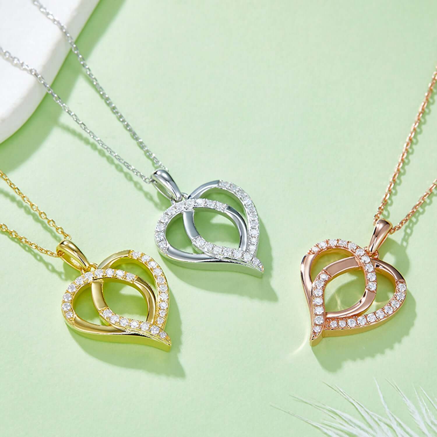 Sterling silver, gold, and rose gold-plated moissanite heart-shaped necklaces on light green background.