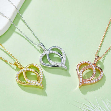 Sterling silver, gold, and rose gold-plated moissanite heart-shaped necklaces on light green background.