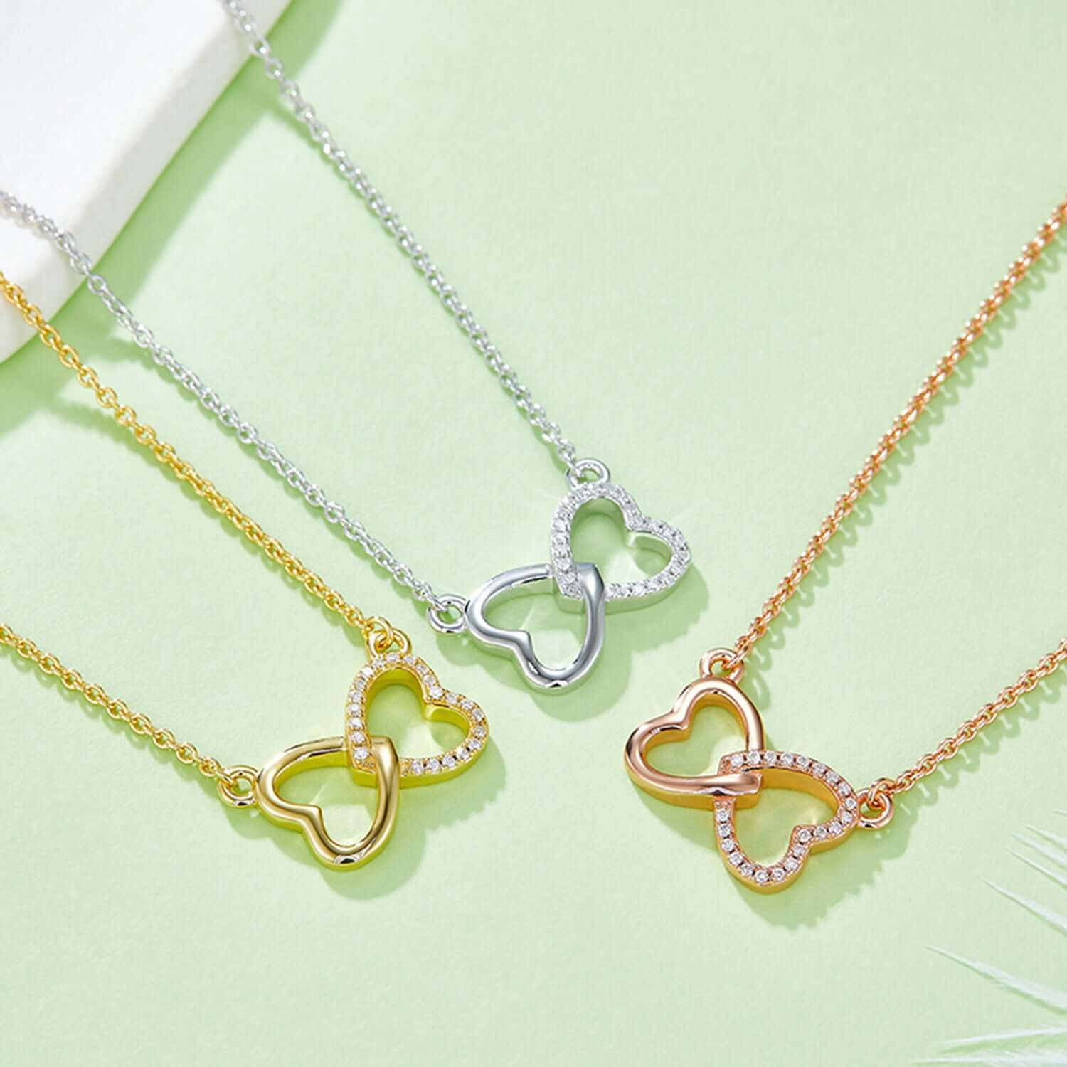 Moissanite 925 sterling silver heart bow necklaces in gold, silver, and rose gold plating on a green background.