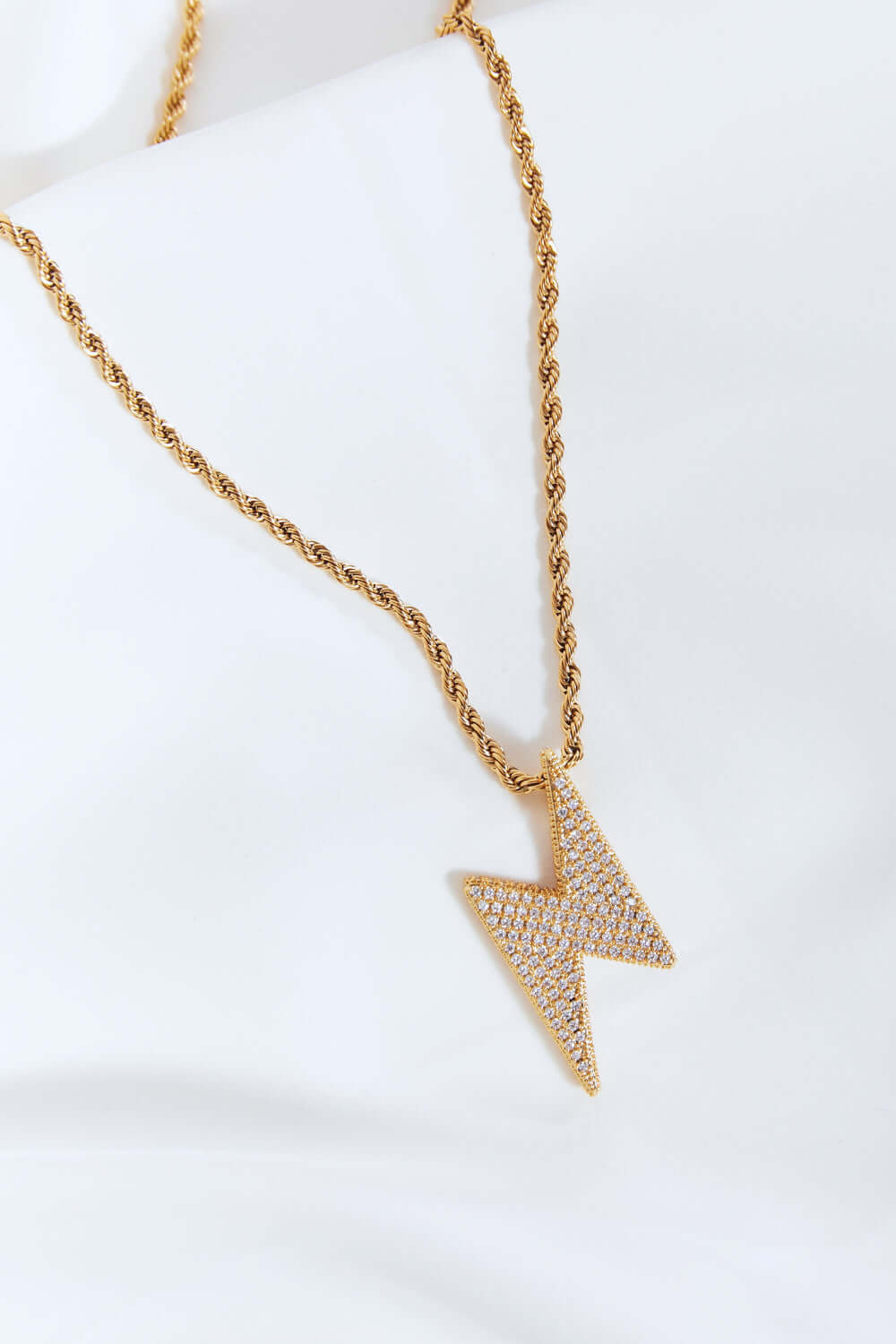 Brass lightning pendant necklace with twisted chain and cubic zirconia detail, flat lay style. Sparkling jewelry on white background.