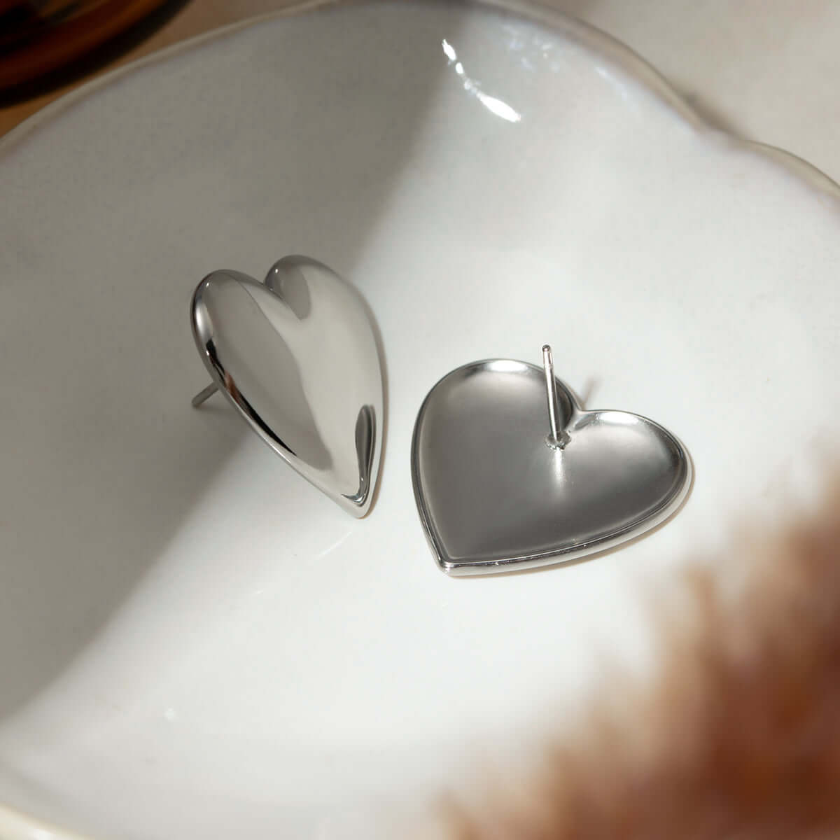 Stainless steel heart-shaped stud earrings on a dish, 18K gold-plated, perfect for everyday wear, elegant and corrosion-resistant.