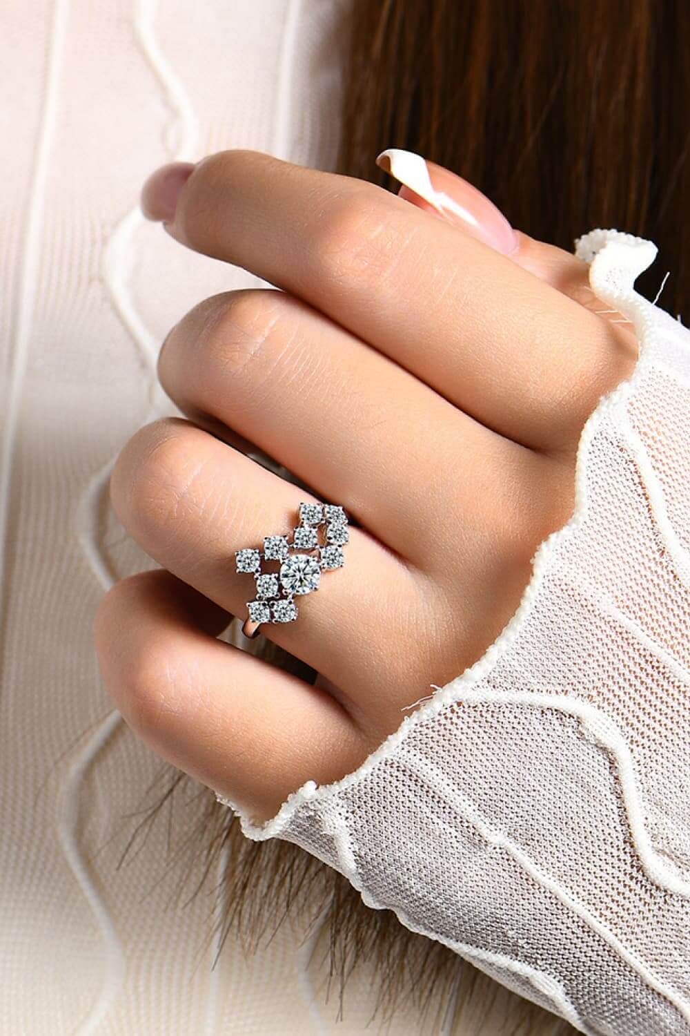 Woman's hand wearing a Moissanite sterling silver ring with intricate design on a white lace background.