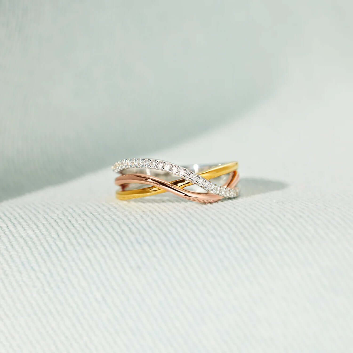 Crisscross gold-plated 925 sterling silver ring with rose gold accents, showcasing elegant design on a soft fabric background.