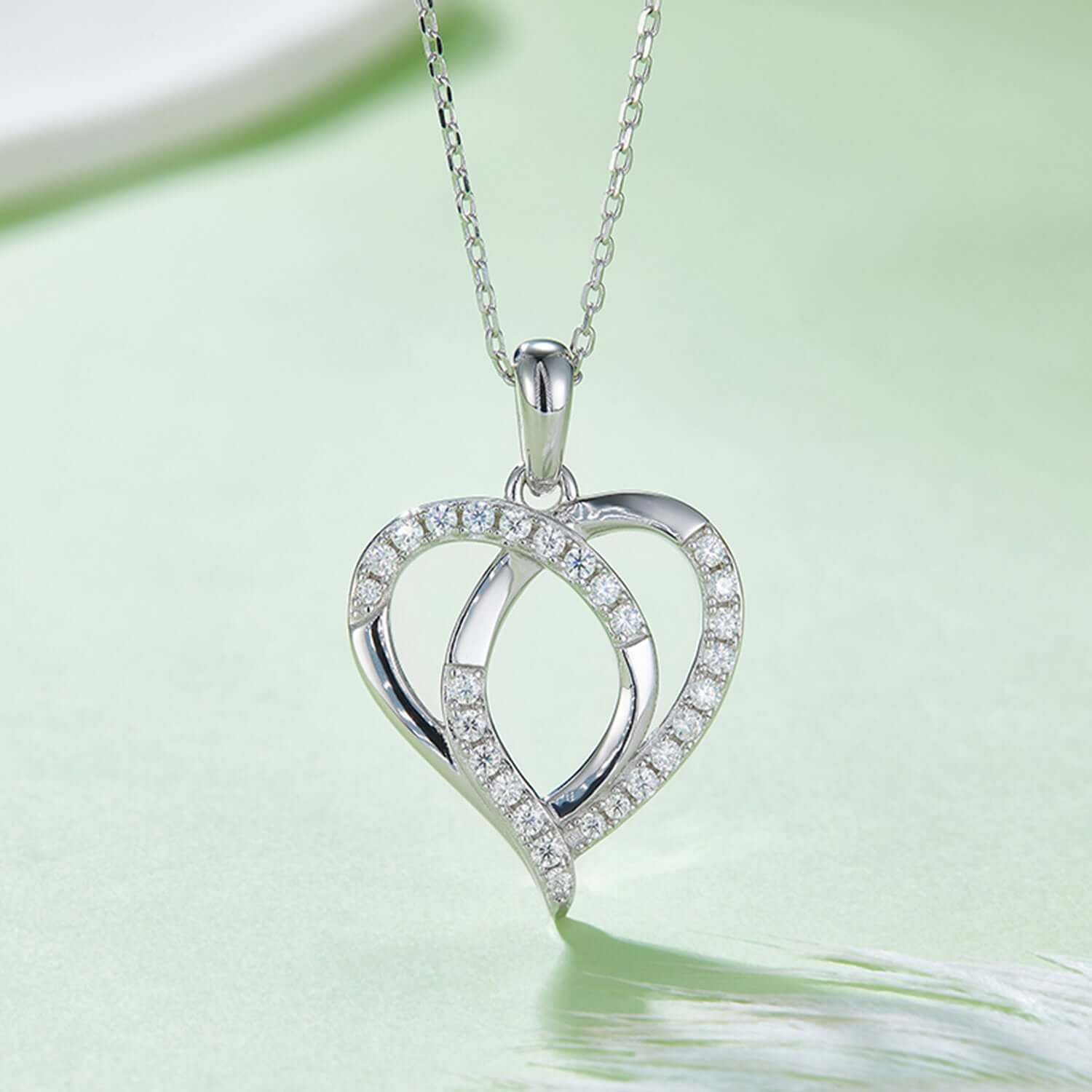 Moissanite 925 sterling silver heart-shaped necklace with rose gold and gold plating, elegant jewelry piece on soft green background.