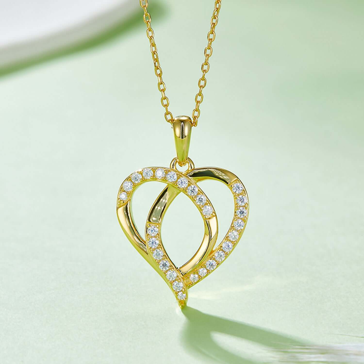 Moissanite heart-shaped necklace in 925 sterling silver, gold-plated with sparkling stones, elegant jewelry piece on green background.