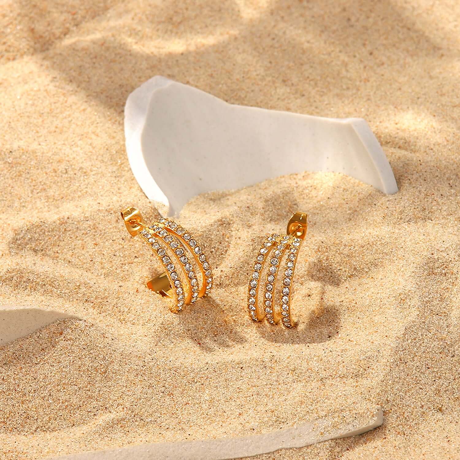 Stainless steel inlaid zircon C-hoop gold-plated earrings on sand with white shell background