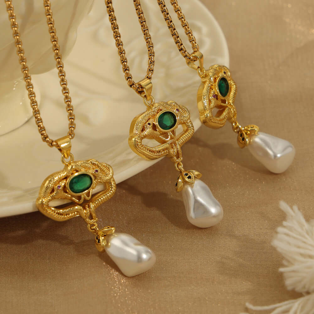 Gold-plated geometric necklaces with freshwater pearls and green glass accents displayed on a beige fabric background.