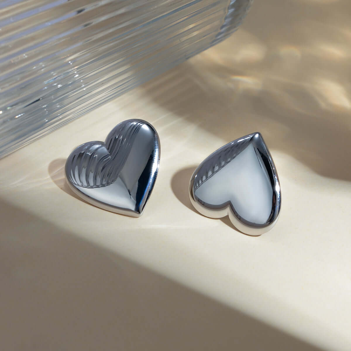 Stainless steel heart stud earrings reflecting light, showcasing their shiny finish and elegant design on a soft surface.