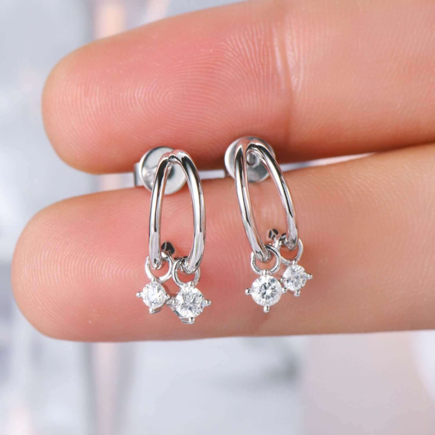 925 sterling silver C-hoop earrings with 0.32 carat moissanite stones, platinum and 18K gold-plated, held by fingers.