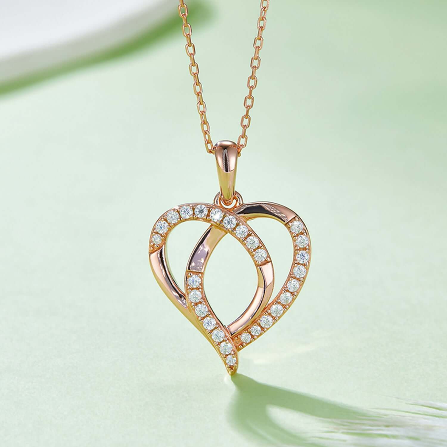 Moissanite 925 sterling silver heart shape necklace with rose gold and gold plating on light green background.