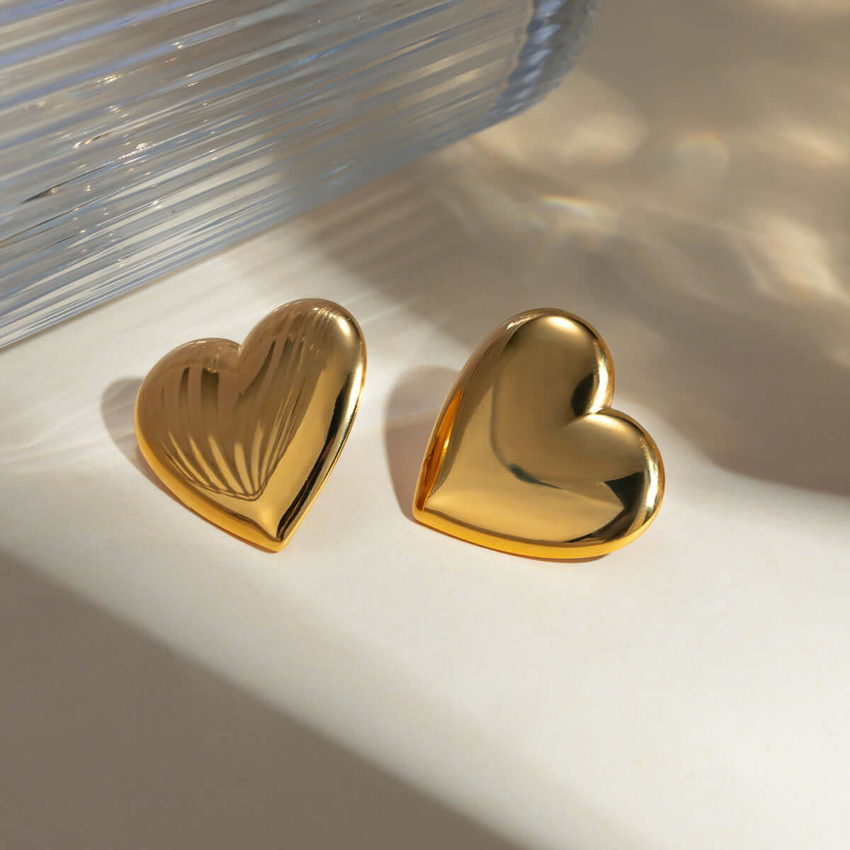 Gold-plated stainless steel heart stud earrings with smooth and textured designs placed on a white surface.