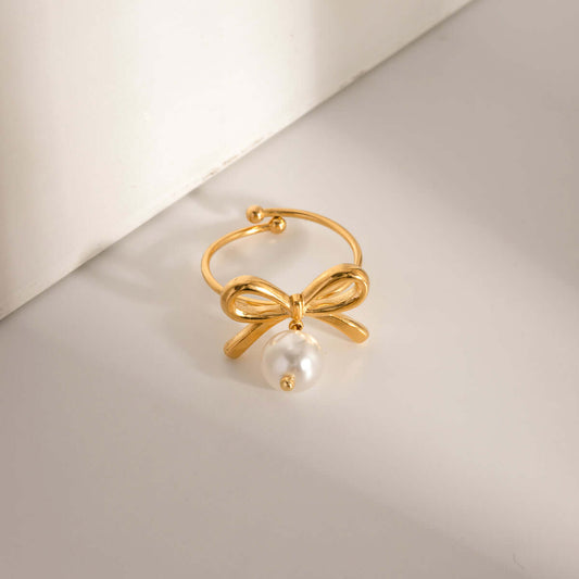 Elegant 18K gold-plated stainless steel ring with synthetic pearl and bow design, adjustable in size, displayed on a light background.