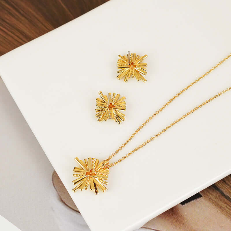 Starburst gold-plated earrings and necklace set with zircon detailing placed on white platform.