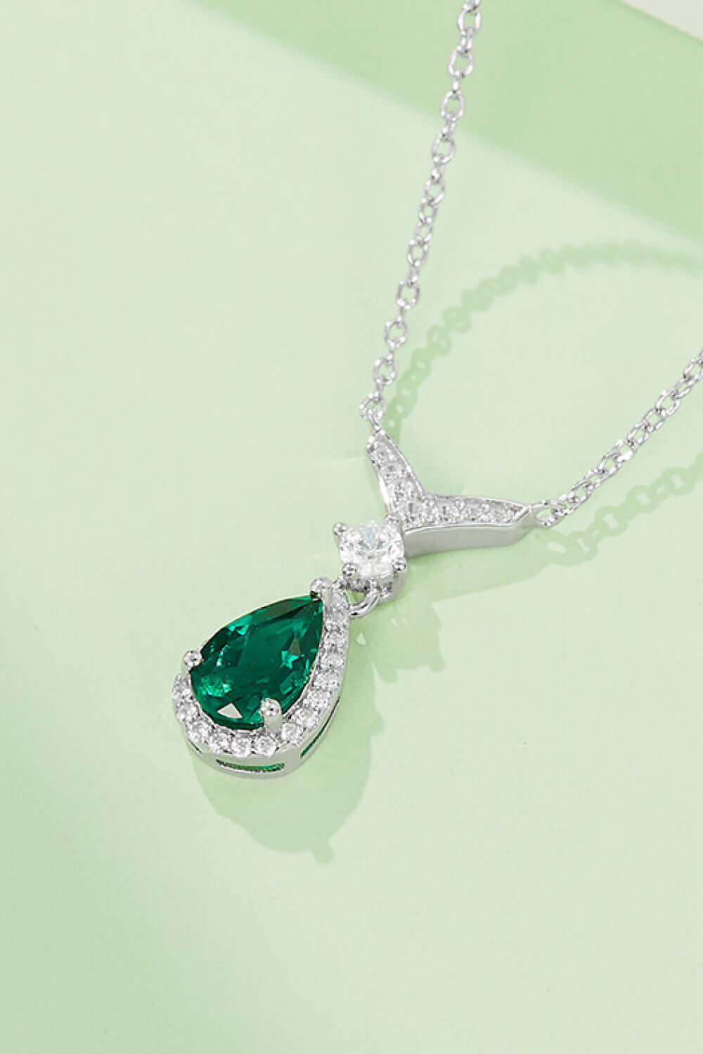 Modern lab-grown emerald teardrop necklace on platinum-plated sterling silver chain displayed on green background.