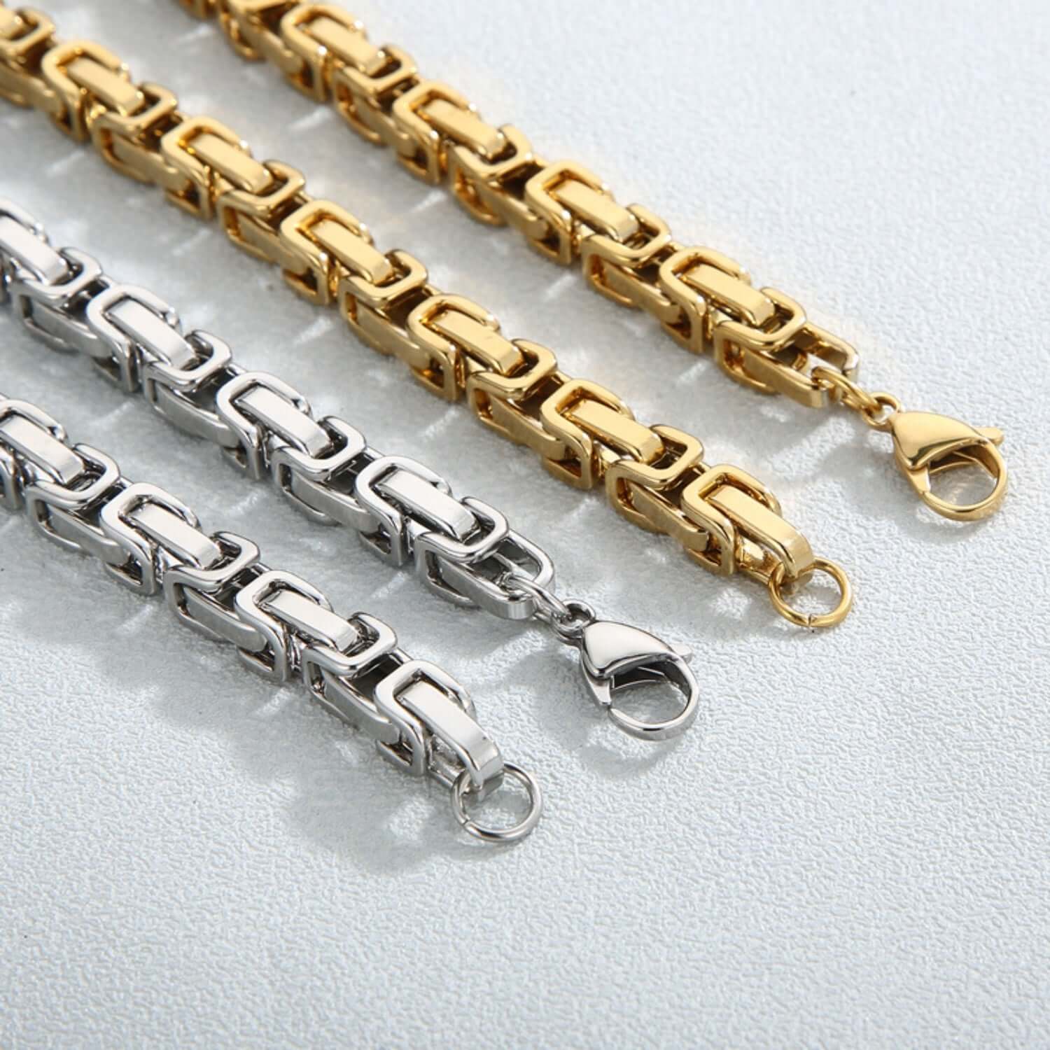 Gold and silver stainless steel bracelets with lobster clasps on a light background