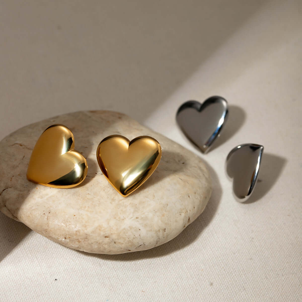 Gold and silver stainless steel heart stud earrings displayed on a stone surface, perfect for a stylish and elegant look.