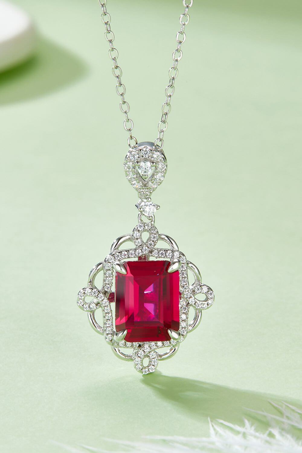 925 sterling silver necklace with a captivating ruby pendant, delicate silver chain, and elegant design displayed on a light green background.