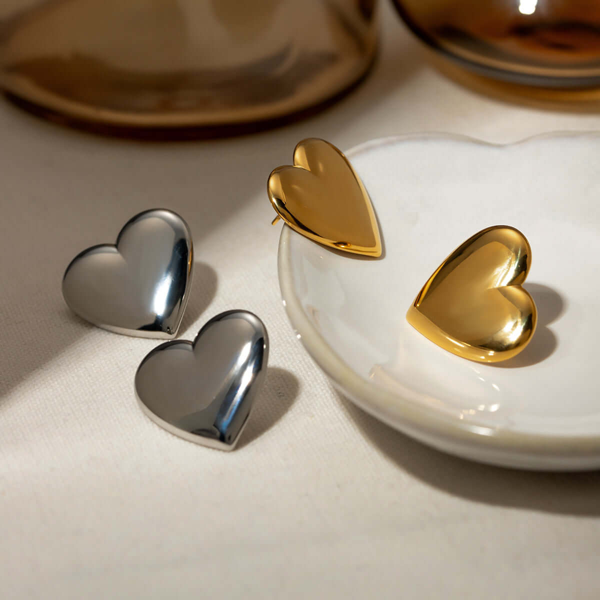 Gold and silver heart stud earrings displayed on a white ceramic dish.